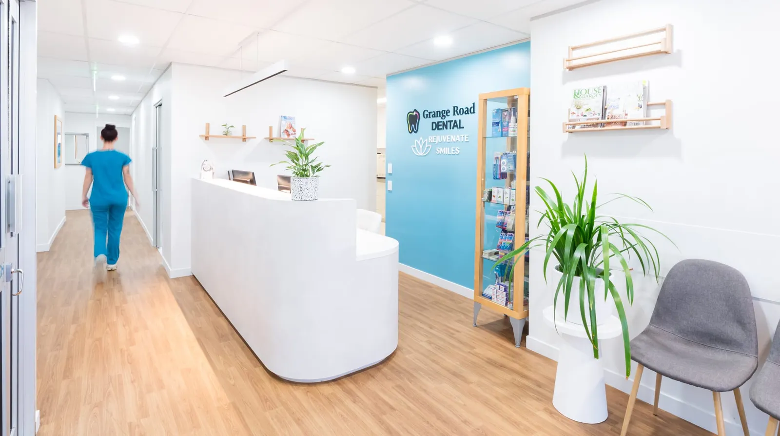 The bright, welcoming reception at Grange Road Dental in Ipswich, with the teal practice sign, a white front desk and a team member walking down the hallway